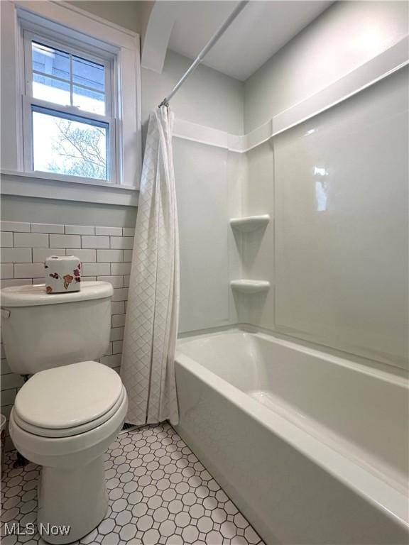 bathroom with shower / tub combo with curtain, tile patterned flooring, tile walls, and toilet