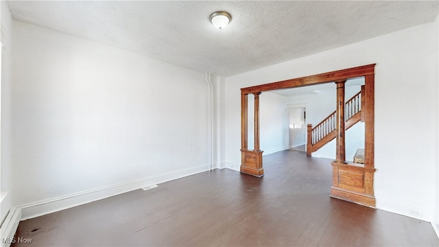 empty room with dark wood-type flooring, a textured ceiling, and decorative columns