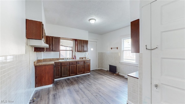 kitchen featuring radiator, light hardwood / wood-style flooring, sink, tile walls, and a textured ceiling