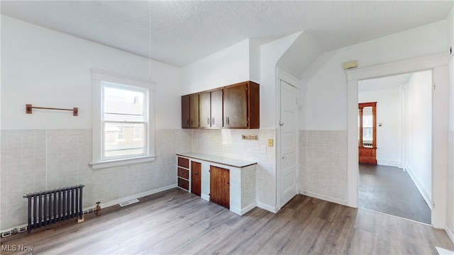 kitchen featuring light hardwood / wood-style flooring, radiator heating unit, dark brown cabinetry, tile walls, and a textured ceiling