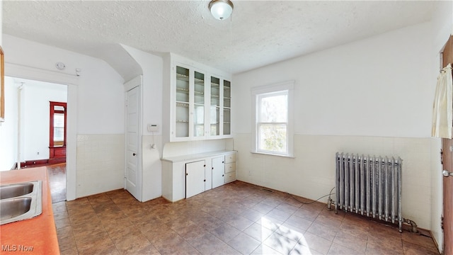 empty room featuring radiator heating unit, a textured ceiling, and tile walls