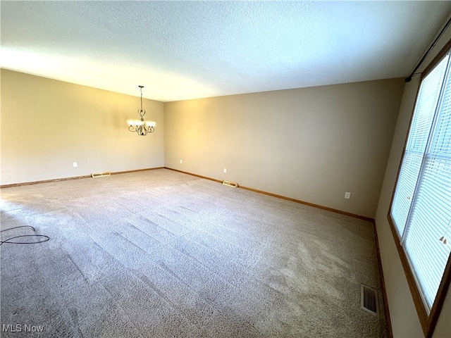 spare room featuring a textured ceiling, an inviting chandelier, and carpet floors