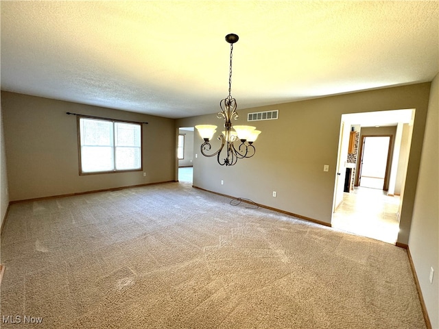 carpeted spare room featuring a textured ceiling and a chandelier