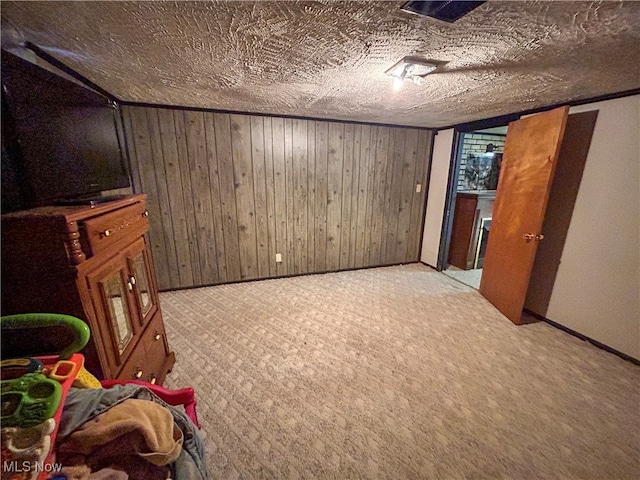 interior space with a textured ceiling, light colored carpet, and wood walls