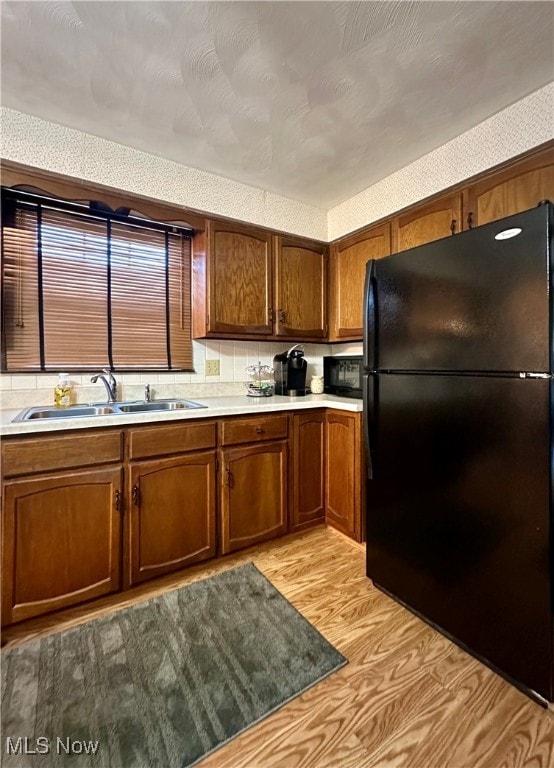 kitchen with light hardwood / wood-style floors, decorative backsplash, black appliances, and sink