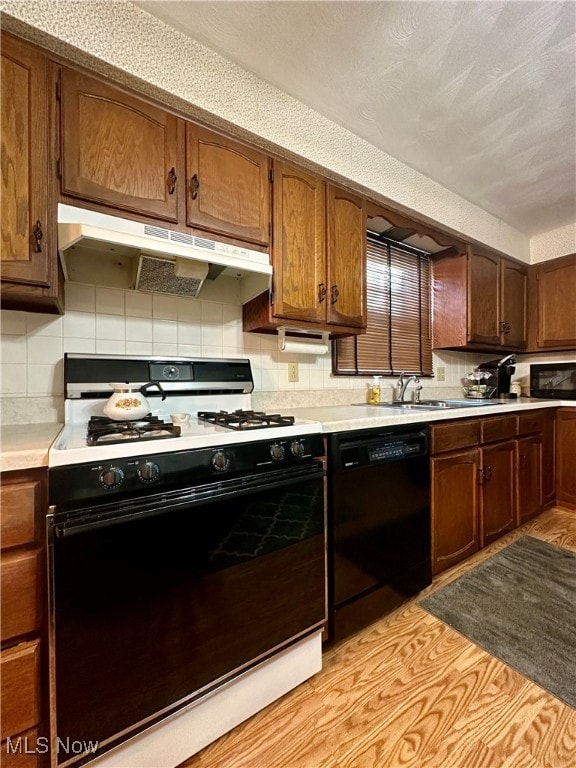 kitchen featuring sink, black appliances, light hardwood / wood-style flooring, and decorative backsplash