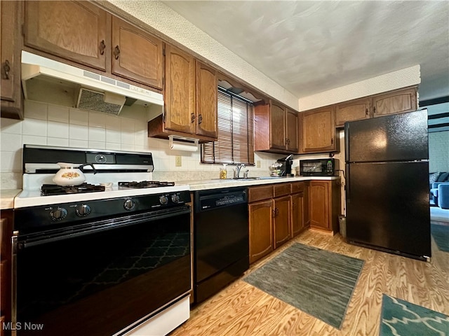 kitchen with sink, black appliances, light hardwood / wood-style flooring, and backsplash