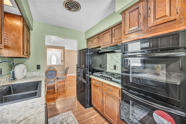 kitchen with light hardwood / wood-style floors, decorative backsplash, black appliances, and sink