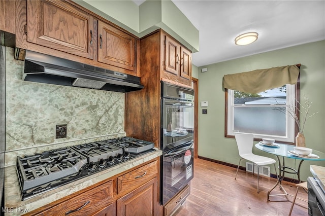 kitchen featuring gas stovetop, double oven, light hardwood / wood-style floors, and tasteful backsplash