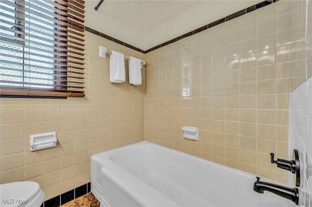 bathroom featuring toilet, plus walk in shower, and tile walls