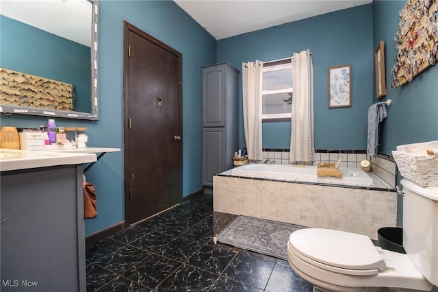 bathroom with vanity, tiled tub, and toilet