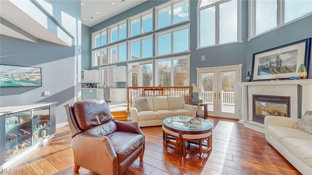 living room with a towering ceiling, french doors, wood-type flooring, and a tile fireplace