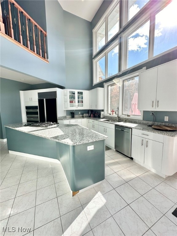 kitchen featuring light stone countertops, a high ceiling, white cabinets, and dishwasher