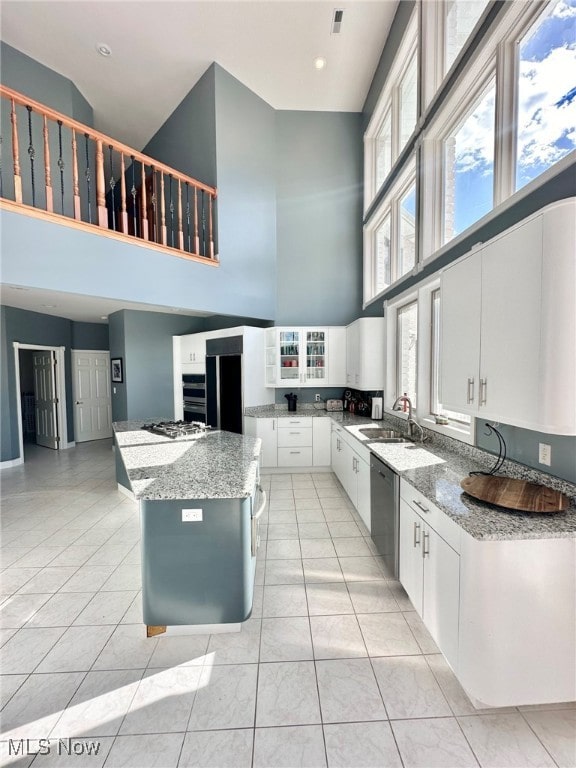 kitchen with white cabinetry, stainless steel appliances, sink, a high ceiling, and a center island