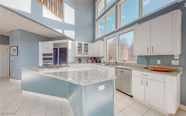 kitchen with a kitchen island, a high ceiling, light stone countertops, white cabinets, and appliances with stainless steel finishes