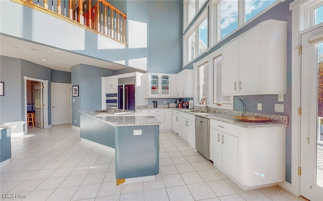 kitchen featuring white cabinetry, stainless steel dishwasher, sink, a high ceiling, and a center island