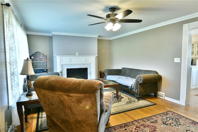 living room with crown molding, a fireplace, light hardwood / wood-style floors, and ceiling fan