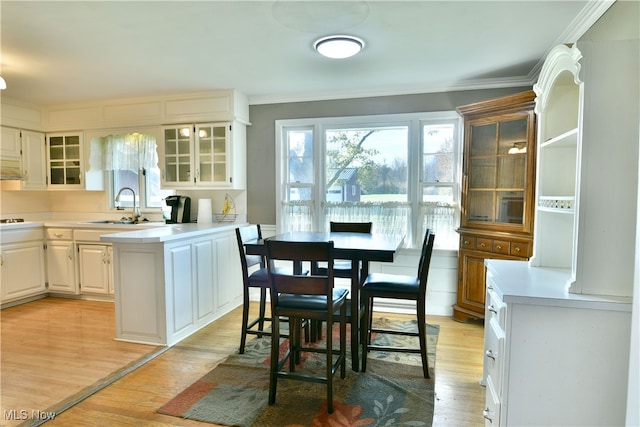 kitchen featuring white cabinetry, crown molding, sink, and light wood-type flooring