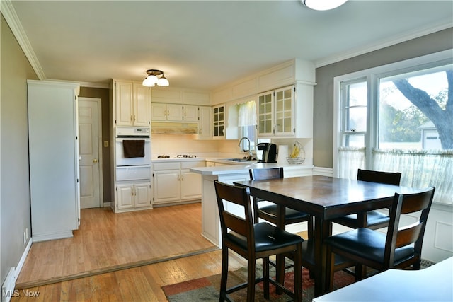 kitchen with white cabinetry, ornamental molding, light hardwood / wood-style floors, sink, and white appliances