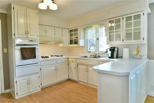 kitchen with backsplash, sink, light wood-type flooring, white cabinets, and white appliances