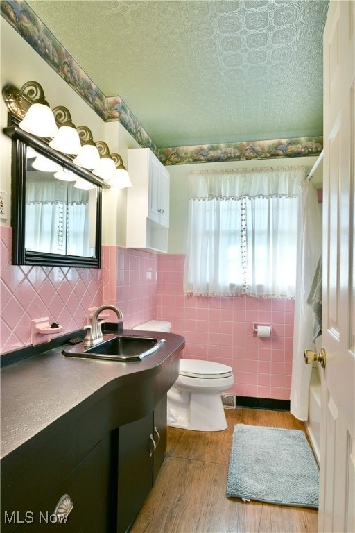 bathroom with toilet, hardwood / wood-style floors, vanity, and tile walls