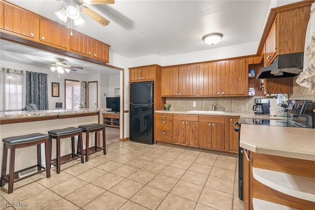 kitchen with black appliances, sink, light tile patterned flooring, decorative backsplash, and a breakfast bar