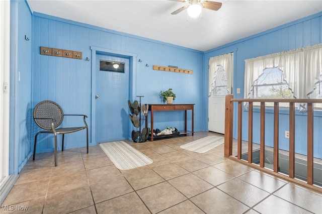 foyer entrance with wood walls, ceiling fan, and tile patterned flooring