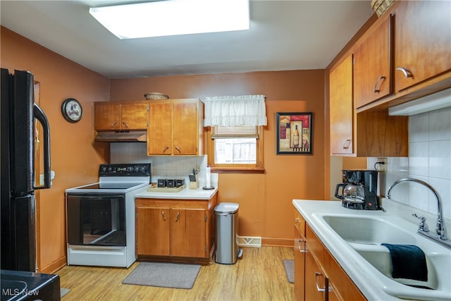 kitchen featuring tasteful backsplash, black fridge, white electric stove, light hardwood / wood-style floors, and sink