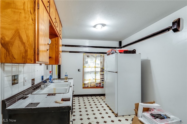 kitchen with backsplash, tile countertops, a textured ceiling, white fridge, and sink