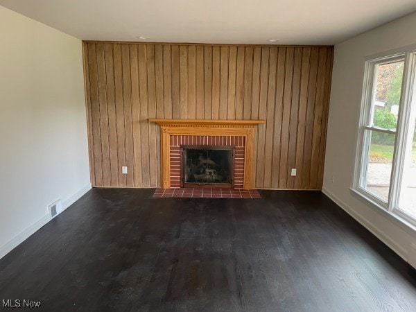 unfurnished living room with wooden walls, a brick fireplace, and dark hardwood / wood-style floors