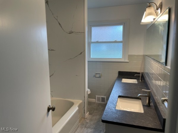 bathroom featuring tile walls, vanity, toilet, and a tub