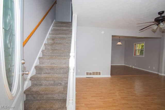 stairway with hardwood / wood-style floors and ceiling fan