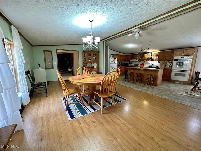 dining room with vaulted ceiling, a textured ceiling, light hardwood / wood-style flooring, and a chandelier