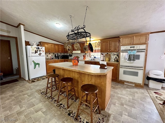 kitchen featuring a kitchen island, backsplash, vaulted ceiling, a textured ceiling, and white appliances