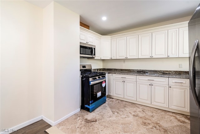 kitchen featuring white cabinets, stainless steel appliances, and dark stone counters