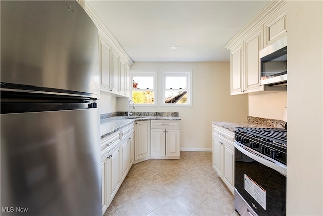 kitchen featuring sink, light stone countertops, white cabinets, light tile patterned floors, and appliances with stainless steel finishes