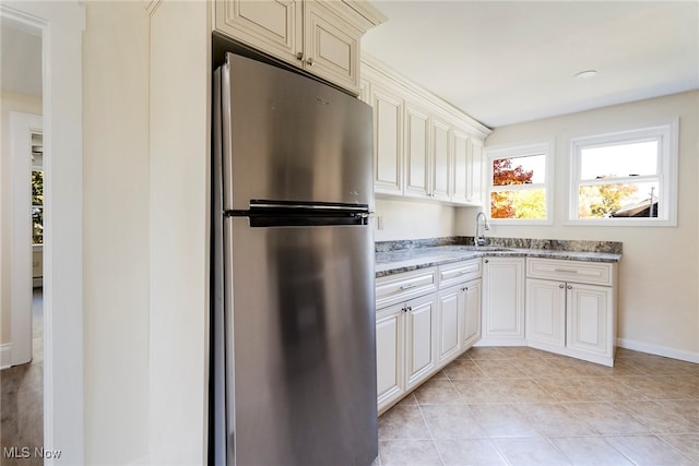 kitchen with stainless steel fridge, light stone countertops, sink, and light tile patterned floors