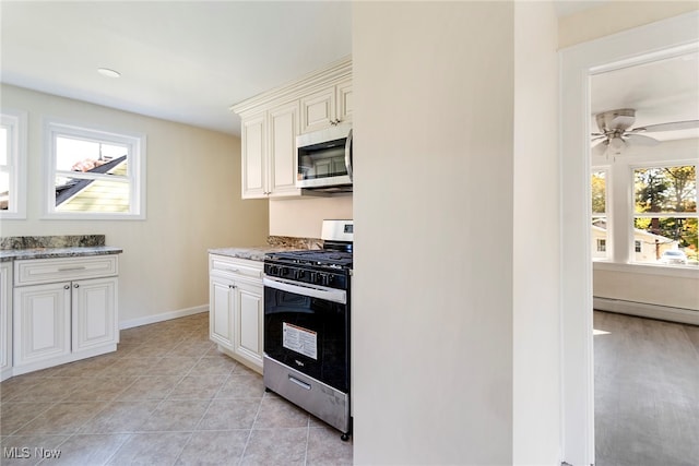 kitchen with light stone counters, appliances with stainless steel finishes, a baseboard heating unit, and white cabinets