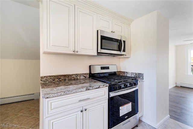 kitchen with appliances with stainless steel finishes, light hardwood / wood-style flooring, dark stone countertops, and baseboard heating