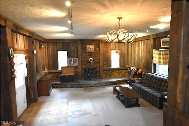 interior space with a wood stove, wooden walls, a textured ceiling, and a notable chandelier