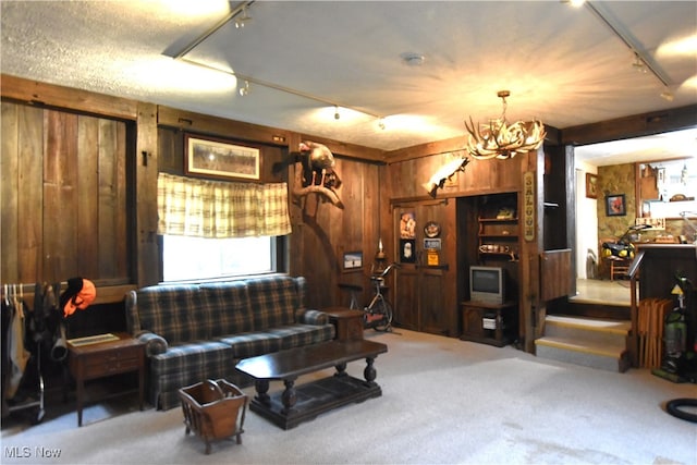 living room with carpet floors, wooden walls, rail lighting, and an inviting chandelier