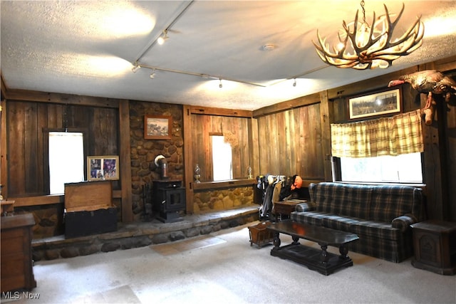 carpeted living room featuring a wood stove, a textured ceiling, wooden walls, and track lighting