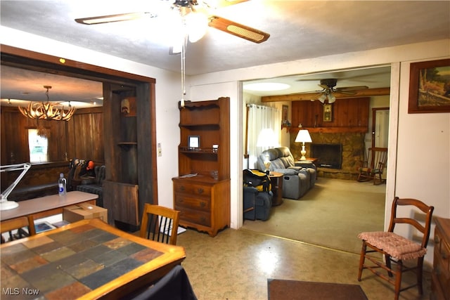 dining area featuring a fireplace, ceiling fan with notable chandelier, and concrete floors