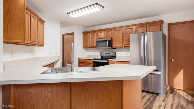 kitchen with light wood-type flooring, appliances with stainless steel finishes, sink, and kitchen peninsula