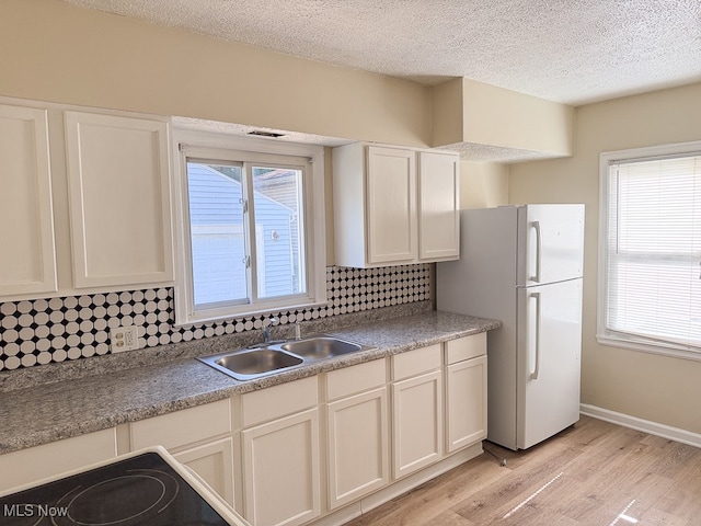 kitchen with sink, white refrigerator, light wood-type flooring, and tasteful backsplash