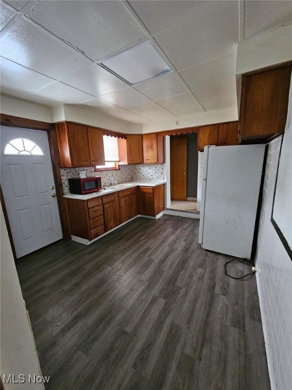 kitchen with white fridge, a paneled ceiling, decorative backsplash, and dark hardwood / wood-style flooring