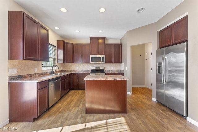 kitchen featuring backsplash, appliances with stainless steel finishes, light hardwood / wood-style flooring, sink, and a center island