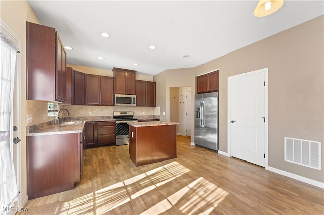 kitchen featuring backsplash, sink, a center island, light wood-type flooring, and appliances with stainless steel finishes