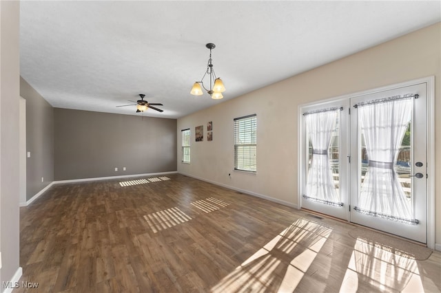 interior space with ceiling fan with notable chandelier, a wealth of natural light, and dark hardwood / wood-style floors