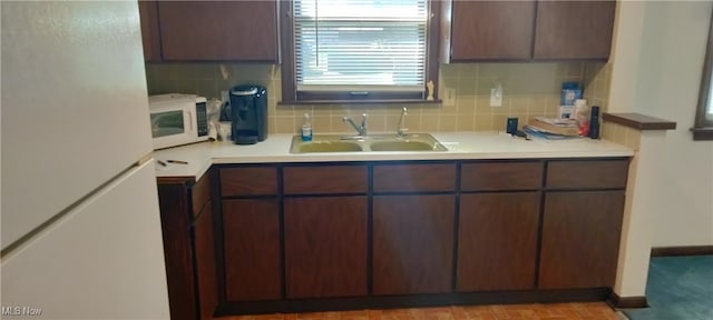 kitchen with backsplash, dark brown cabinetry, sink, and white appliances